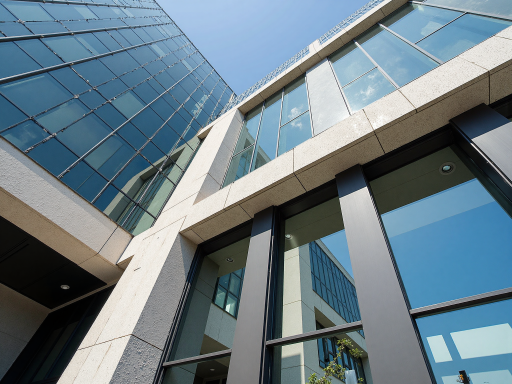 现代化办公大楼外景,玻璃幕墙设计,阳光照射下呈现科技感,周围绿植环绕